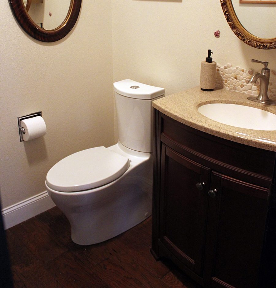 A half bath with a white toilet, a dark wood vanity with a speckled top and a pebble-tile splash.