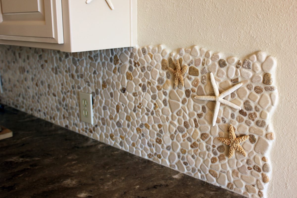 A pebble-tile backsplash with two starfish set into it, above a dark stone counter.