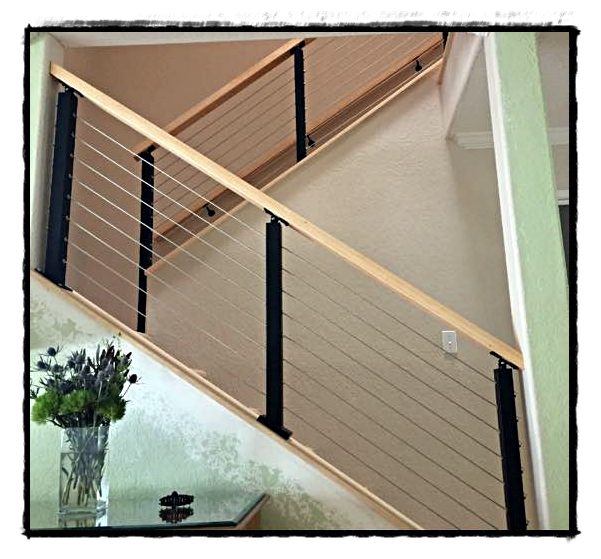A stair with a cable railing and a light wood handrail.